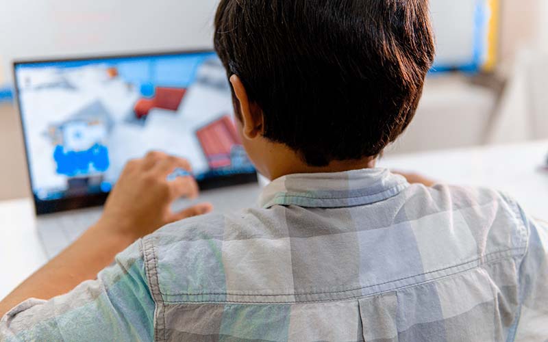Elementary-aged boy playing video game on laptop in classroom